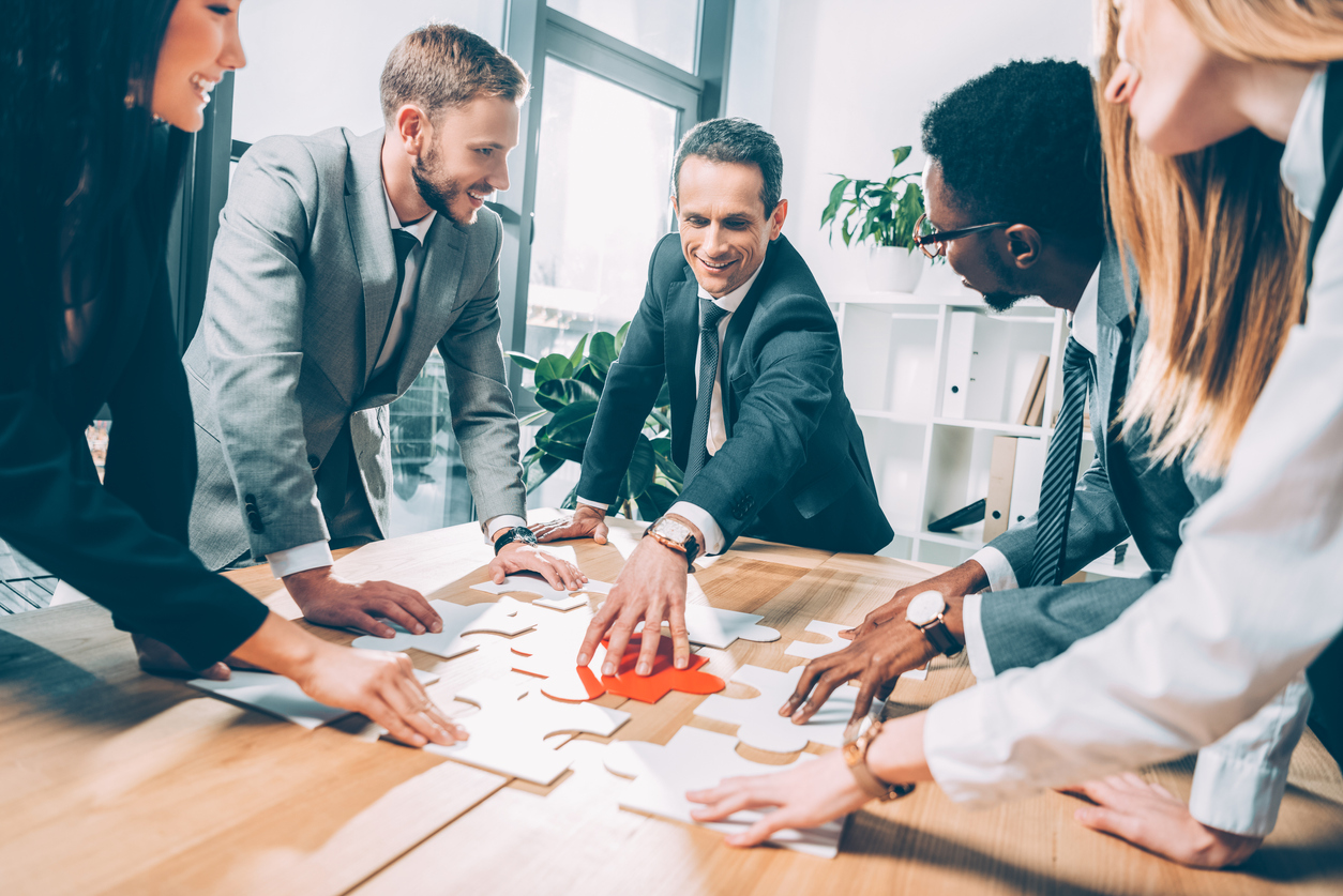 Diverse group of businesspeople putting pieces of a puzzle together, showing a concept of building a sales strategy.