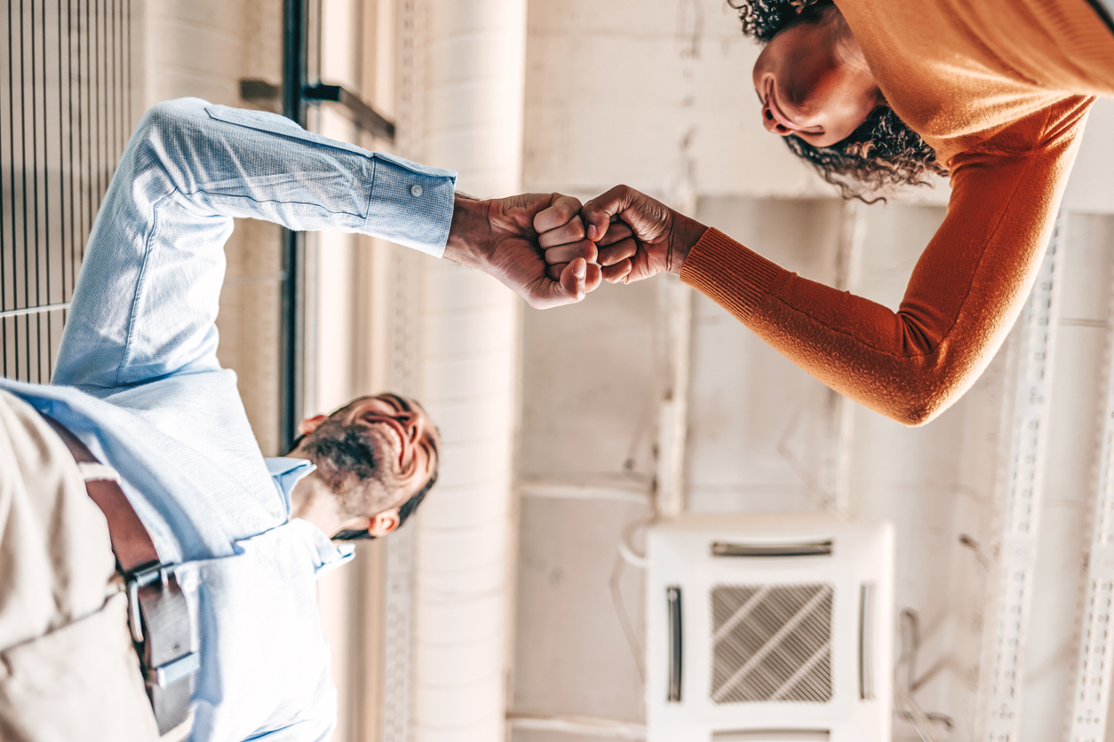 Two salespeople in an office fist bumping each other, celebrating accomplishments with their company's sales.